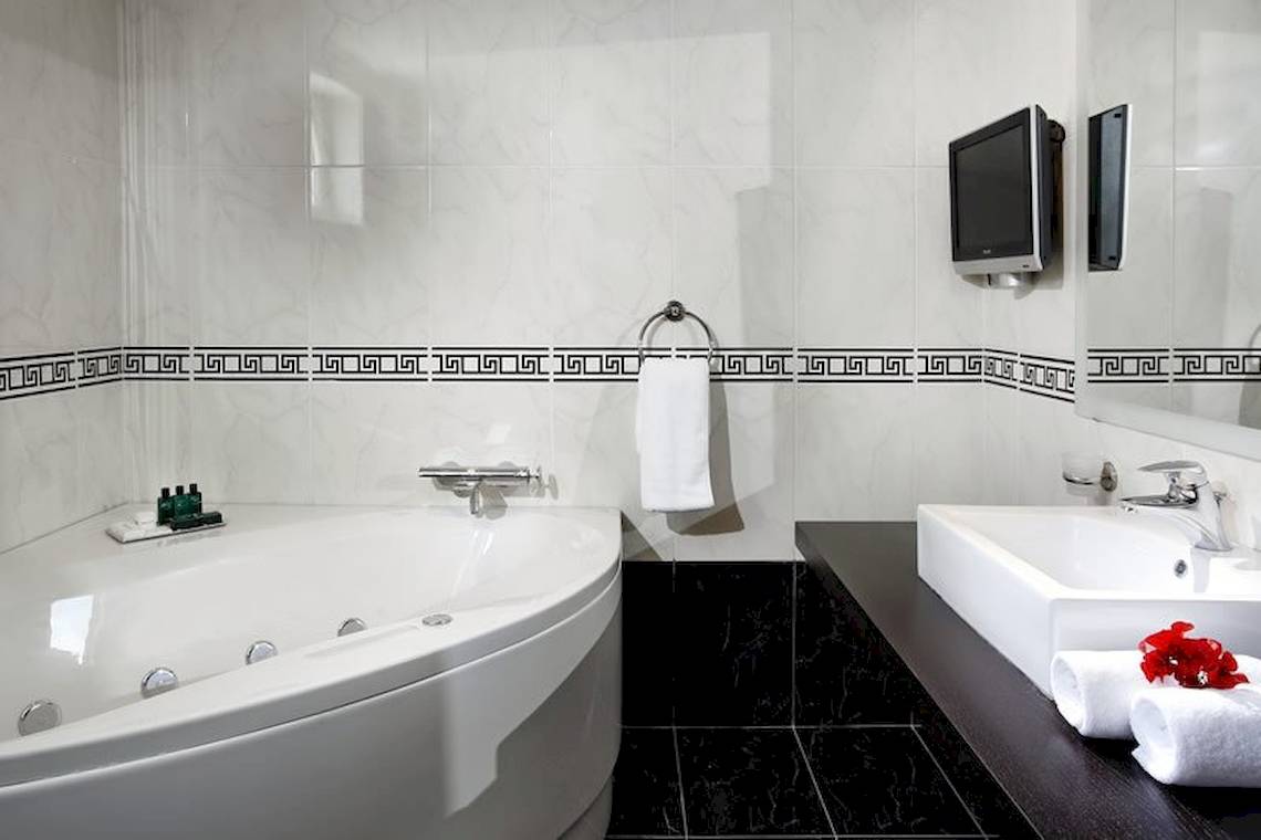 Badezimmer im Olympia Golden Beach Resort mit Badewanne, Waschbecken und Fernseher an der Wand.