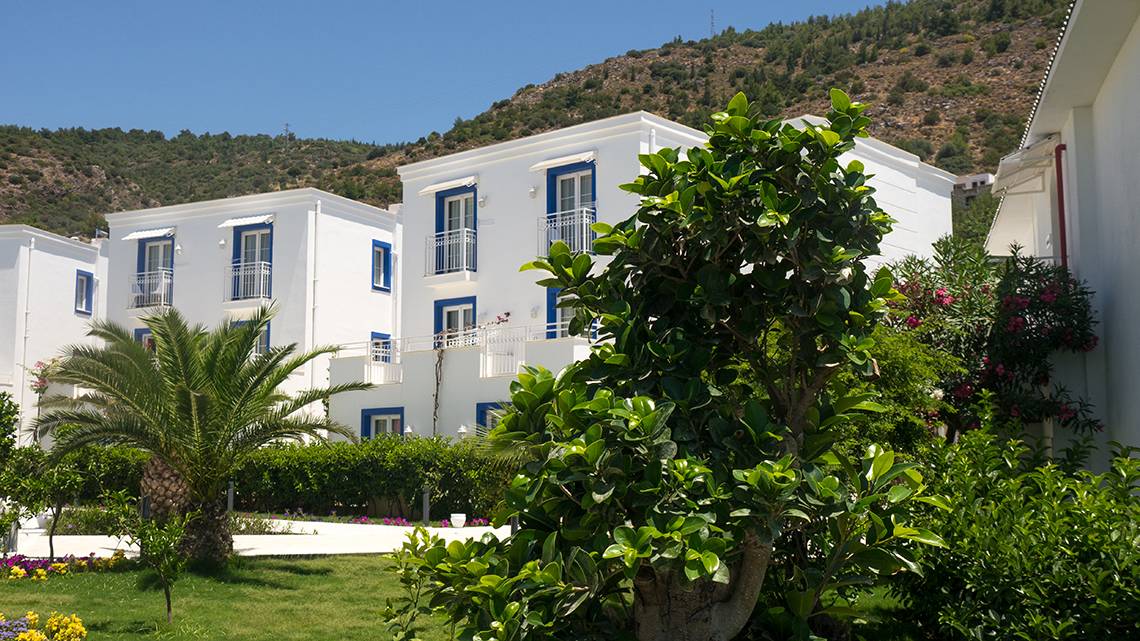 Außenansicht des Labranda TMT Bodrum Hotels mit weißen Gebäuden, blauen Fensterrahmen und umliegenden Pflanzen.