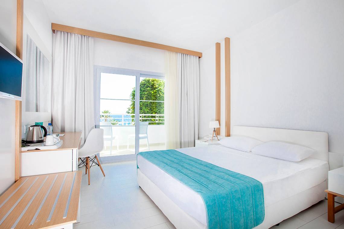 Foto von einem weißen Hotelzimmer mit einem Bett, Fernseher, Schreibtisch und einem Balkon