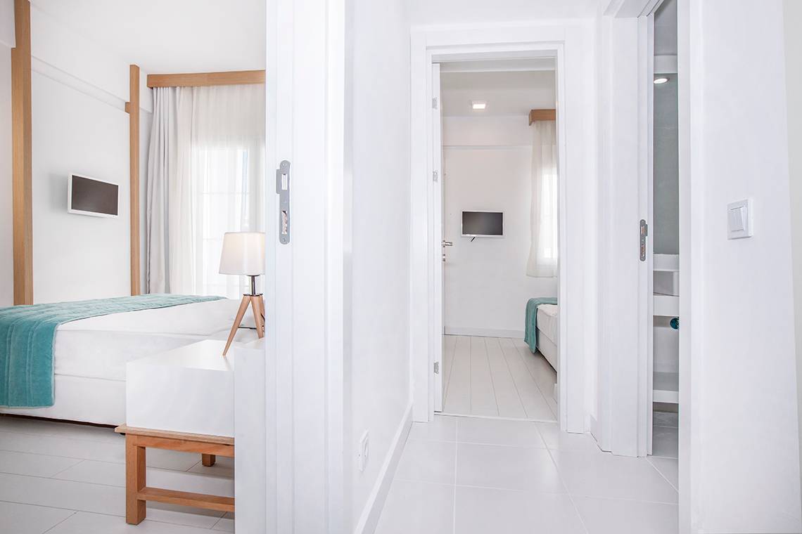 Innenansicht eines Zimmers im Labranda TMT Bodrum Hotel mit weißem Interieur, Bett, Tisch und Fernseher.