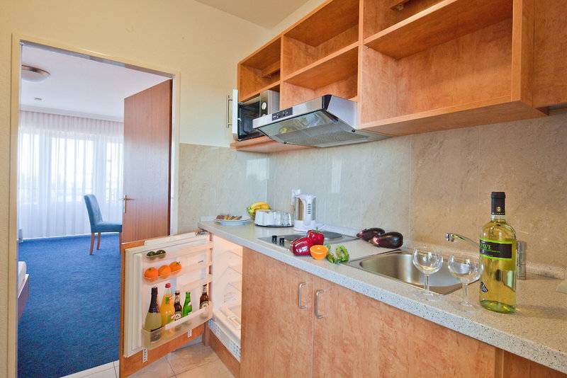 Küche im Zimmer des Hamburg Mitte Hotels mit Kühlschrank, Mikrowelle, Obst und Weinflasche.