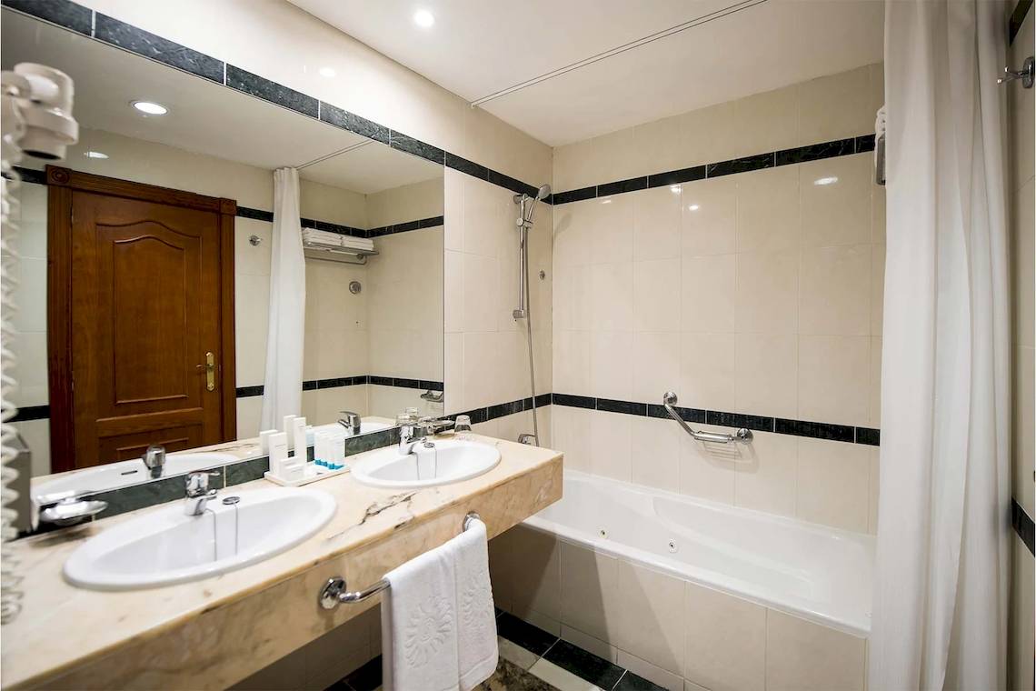 Ein Badezimmer im Bahia Principe Sunlight Costa Adeje mit einer Badewanne, zwei Waschbecken und einem großen Spiegel.