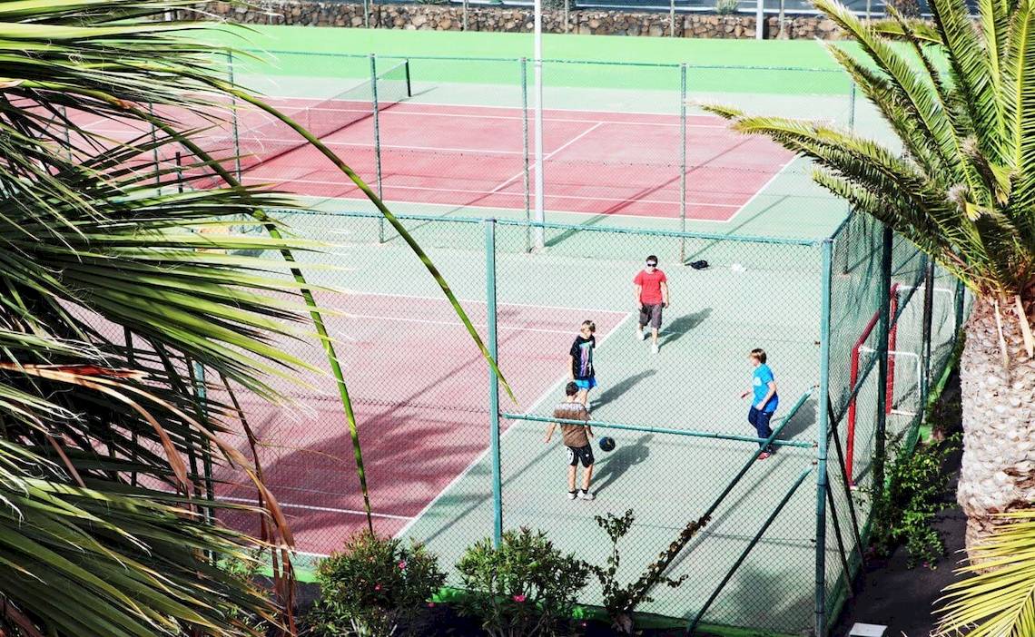 Tennisplatz im Hotel H10 Suites Lanzarote Gardens mit mehreren Spielern und Palmen im Hintergrund.
