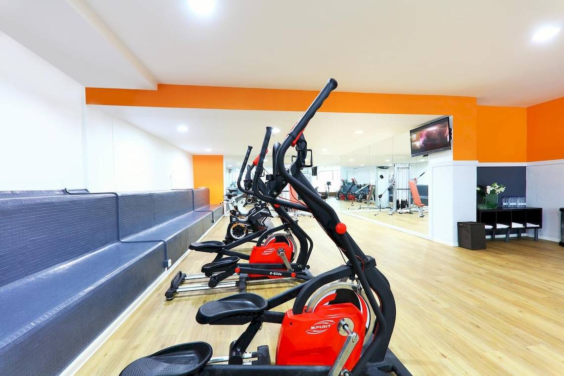 Fitnessstudio im Iberostar Malaga Playa Hotel mit rot-schwarzen Crosstrainern und Spiegelwand.