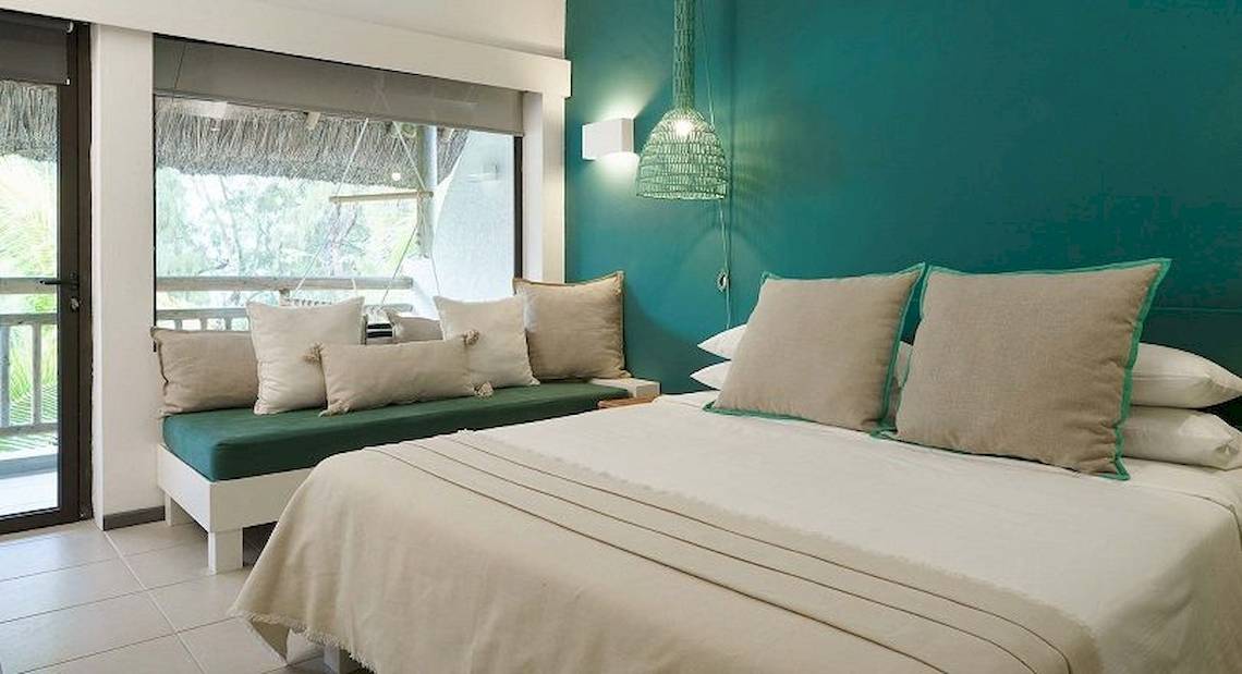 Schlafzimmer des Recif Attitude Hotels mit blauer Wand, Doppelbett, Kissen und Fenster mit Balkon.