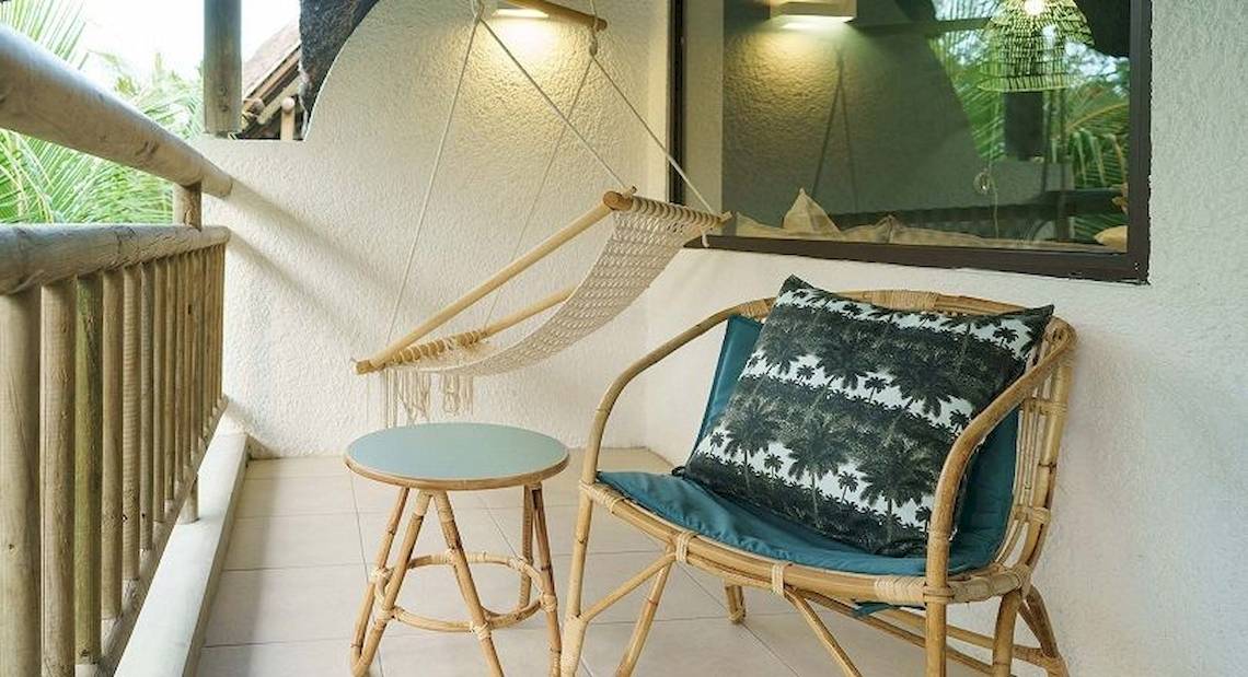 Balkon des Recif Attitude Hotels mit Korbstuhl, Kissen, kleinem Tisch und Seilschaukel.