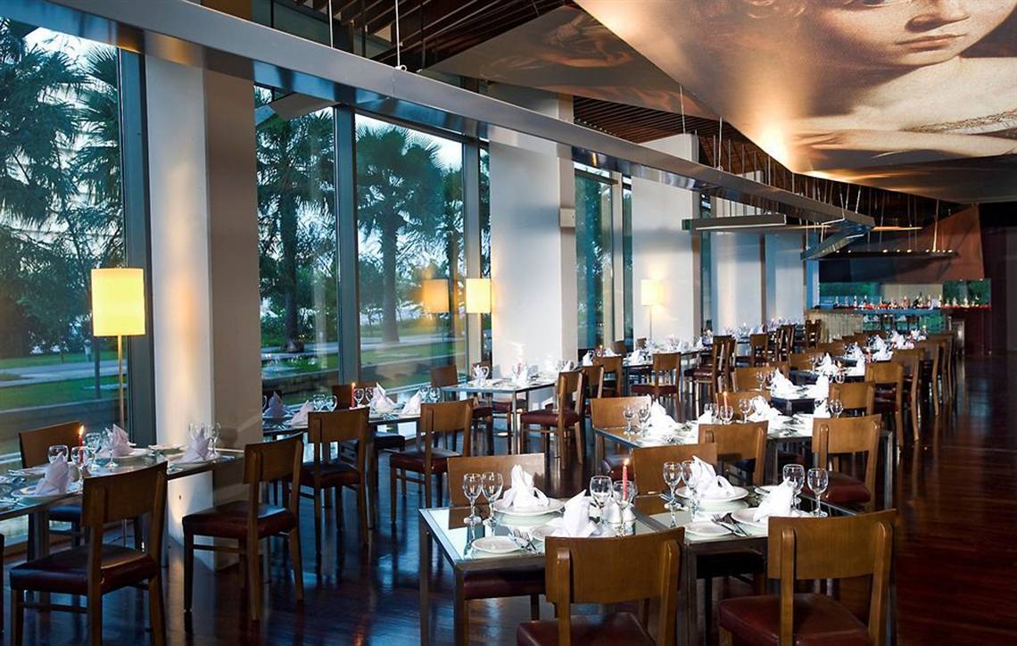 Innenansicht des Restaurants im Nirvana Cosmopolitan Hotel mit vollen Tischen und einer großen Wandmalerei.