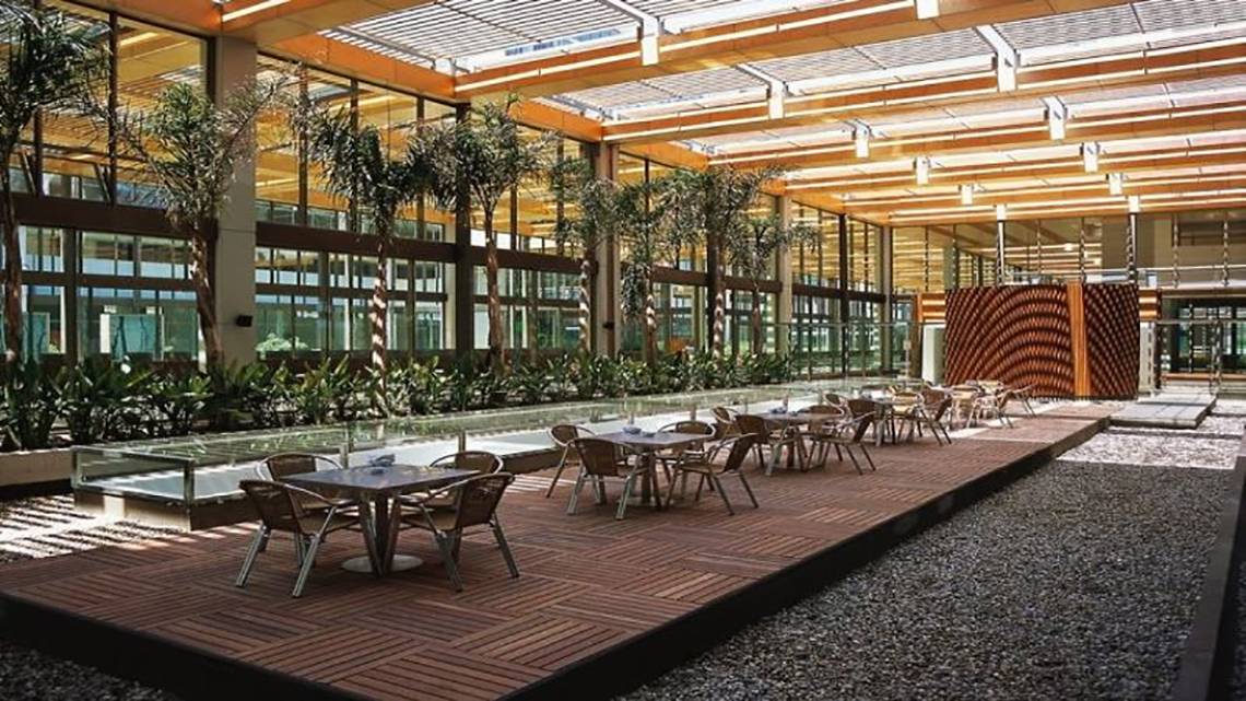 Innenhof des Nirvana Cosmopolitan Hotels mit Tischen und Stühlen, umgeben von Pflanzen und großen Fenstern.