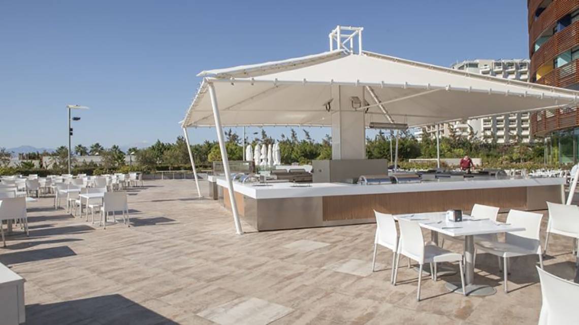 Foto der Terrasse des Nirvana Cosmopolitan Hotels mit einer großen weißen Überdachung und vielen weißen Tischen und Stühlen.