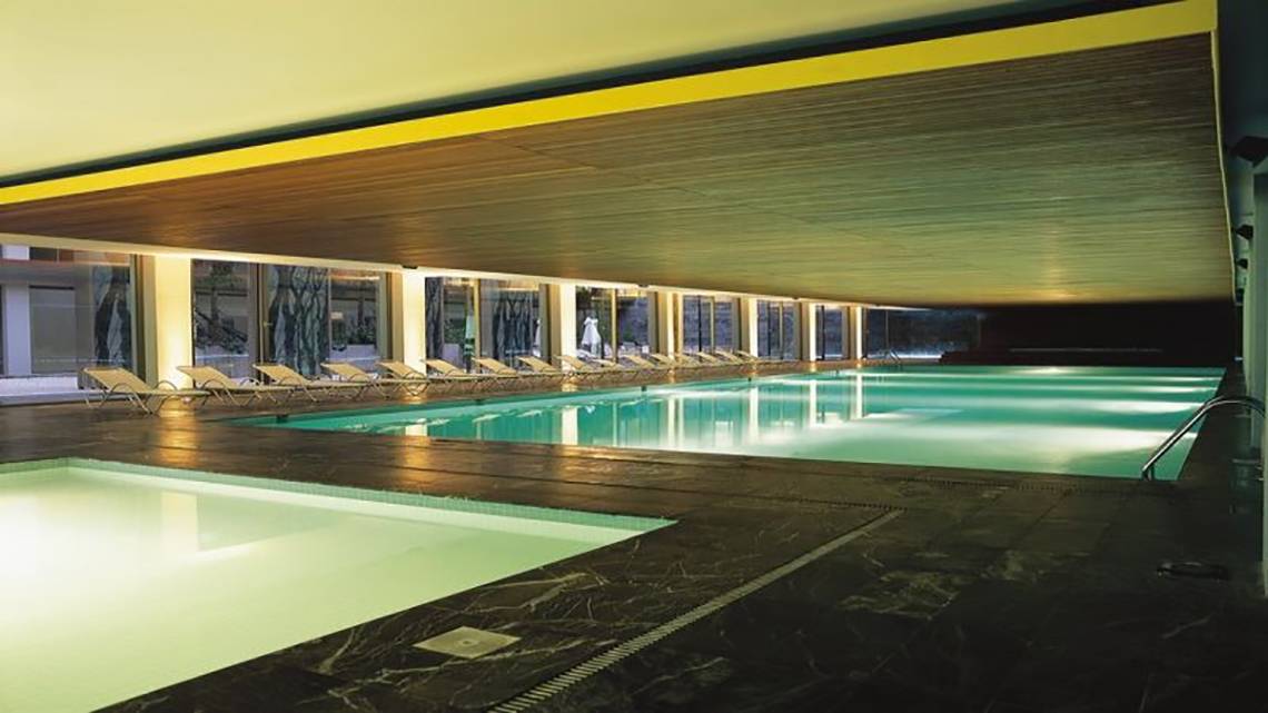 Innenpool des Nirvana Cosmopolitan Hotel mit Lounge-Sesseln und heller Beleuchtung.