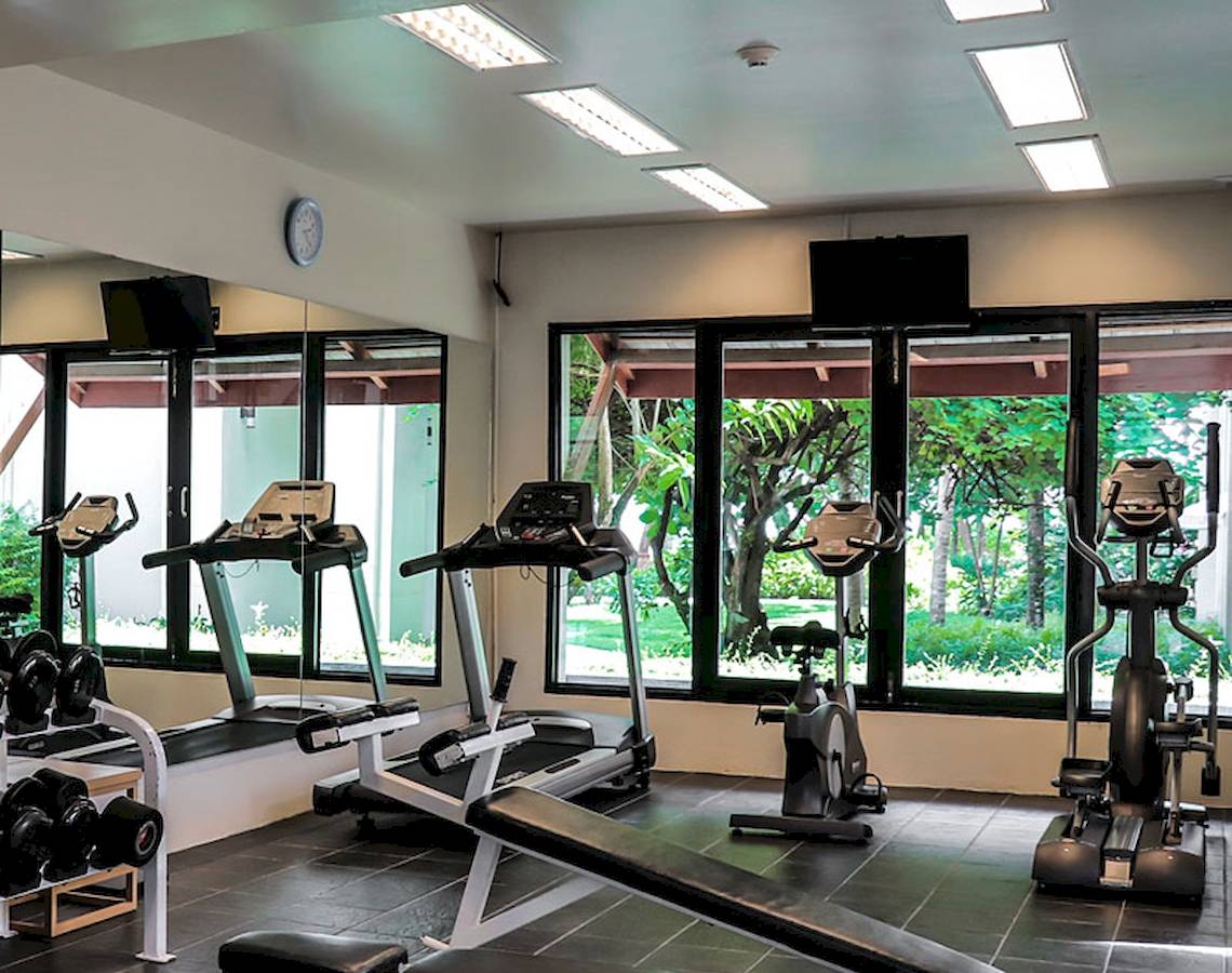 Fitness Center im Apsara Beachfront Resort und Villa mit Geräten und Fenstern.