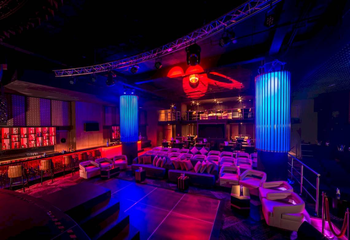 Lounge-Bereich im Hotel mit blauen und roten Lichtern, Sofas und einer Bar.
