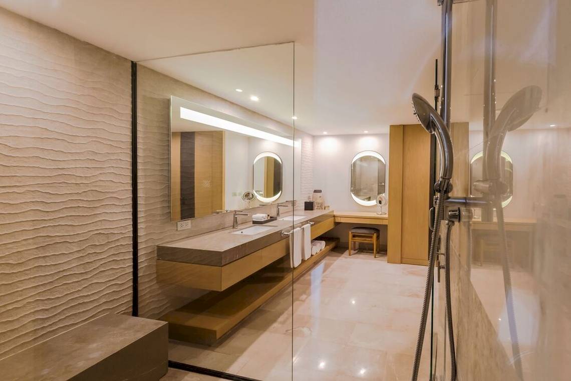 Badezimmer im Haven Riviera Cancun Resort & Spa mit Marmorboden, Glasdusche und zwei Waschbecken.