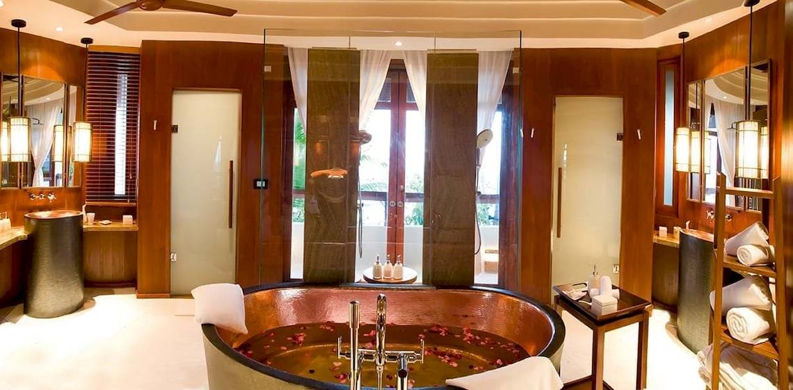 Badezimmer im Constance Halaveli Maldives mit großer Badewanne, Holzwänden und Glastür.