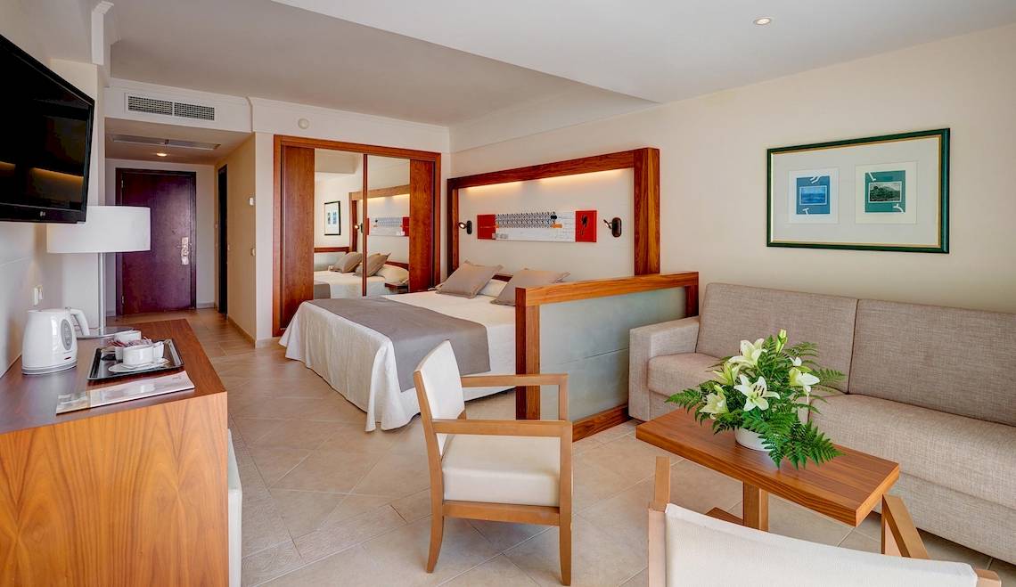 Innenansicht eines Hotelzimmers im Hipotels Natura Palace mit Bett, Sofa, Tisch und Fernseher.