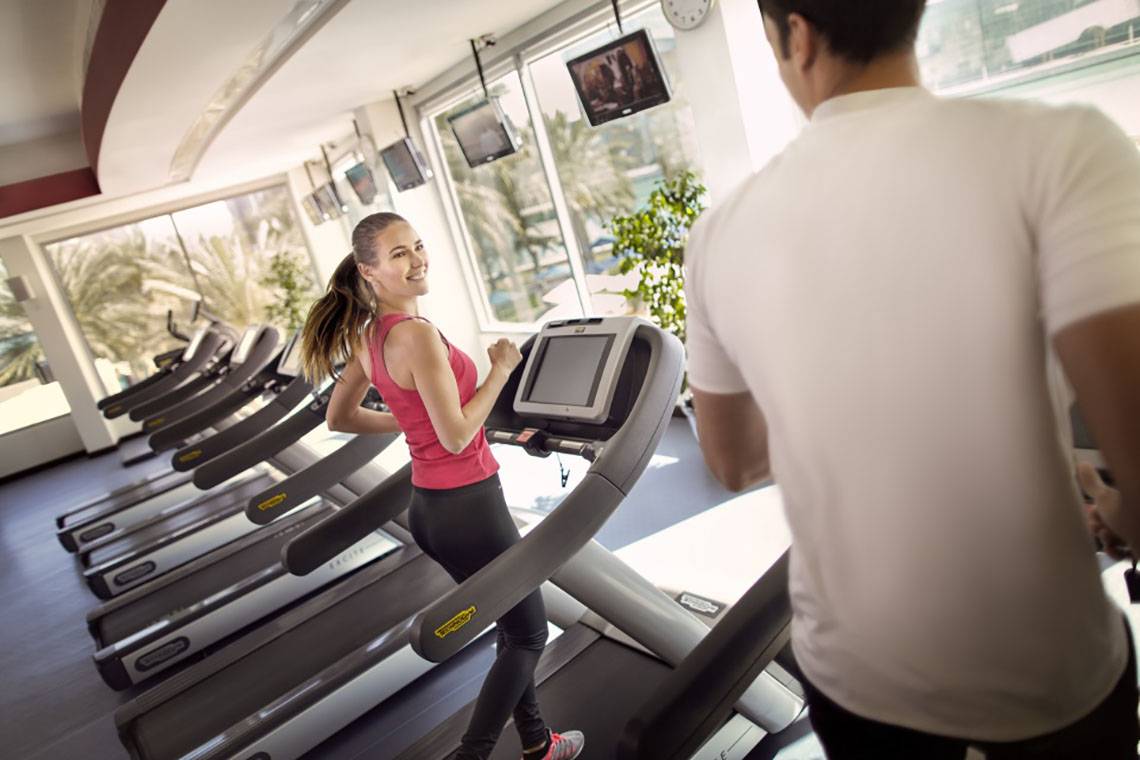 Frau im Fitnessstudio auf dem Laufband läuf, während ein Mann ihr zuschaut