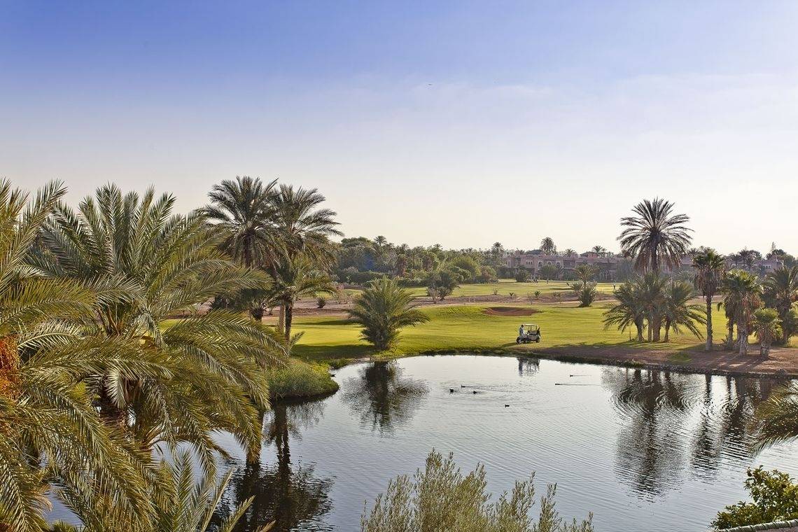 Aussicht auf den Golfplatz des Palmeraie Palace mit einem Golfwagen und einem See.