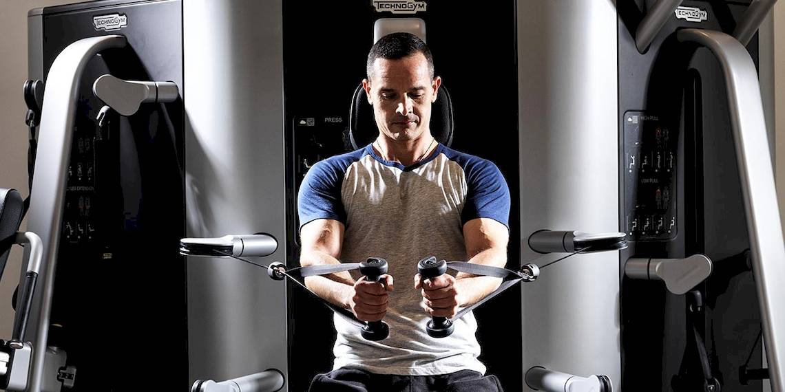 Mann im Fitnessstudio beim Training mit Hanteln an einem Kraftgerät.