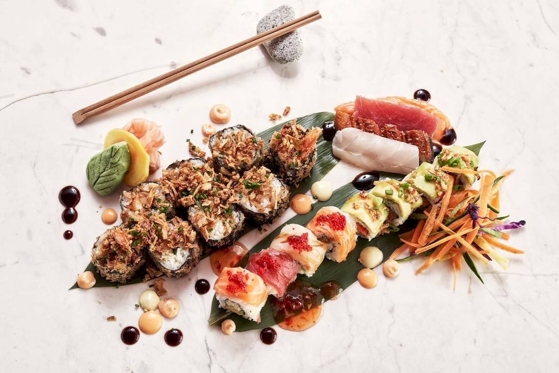 Verschiedene Sushi-Rollen auf einer Marmorplatte mit Sojasauce und Essstäbchen.
