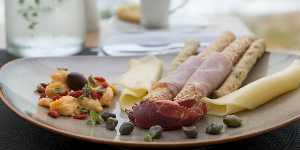 Ein Teller mit Käse, Aufschnitt, Oliven, Kapern und Gewürzen im Myconian Korali Hotel.