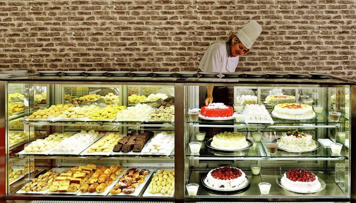 Eine Konditorin im Side Royal Paradise Hotel bereitet Kuchen zu, die in einer Vitrine ausgestellt sind.