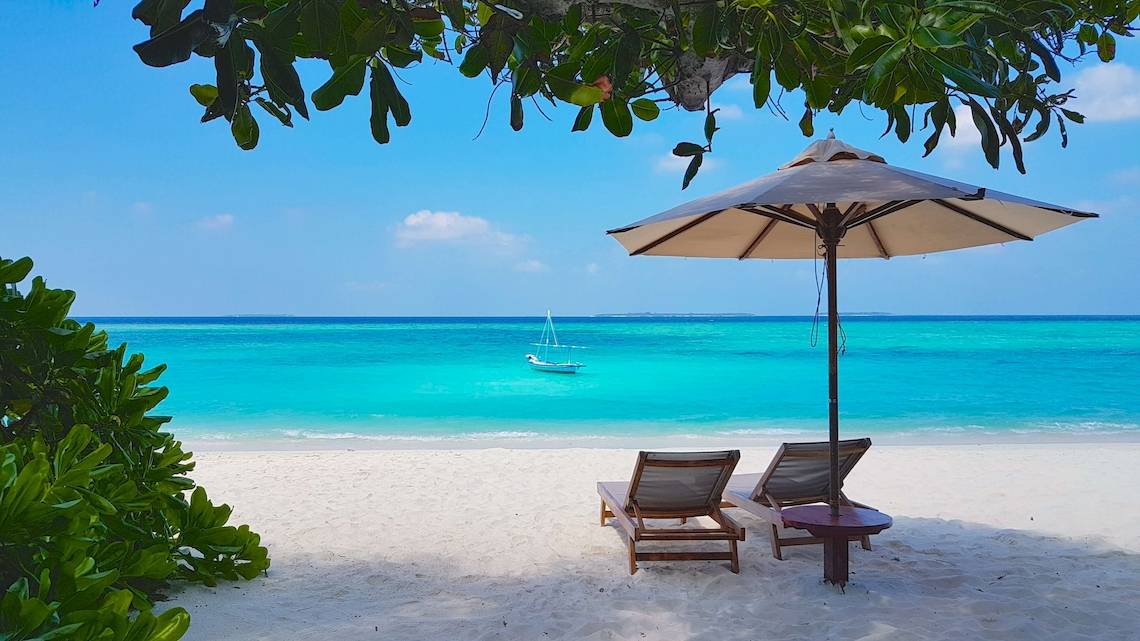 Strand mit Sonnenschirm, zwei Liegen und einem Boot im Wasser