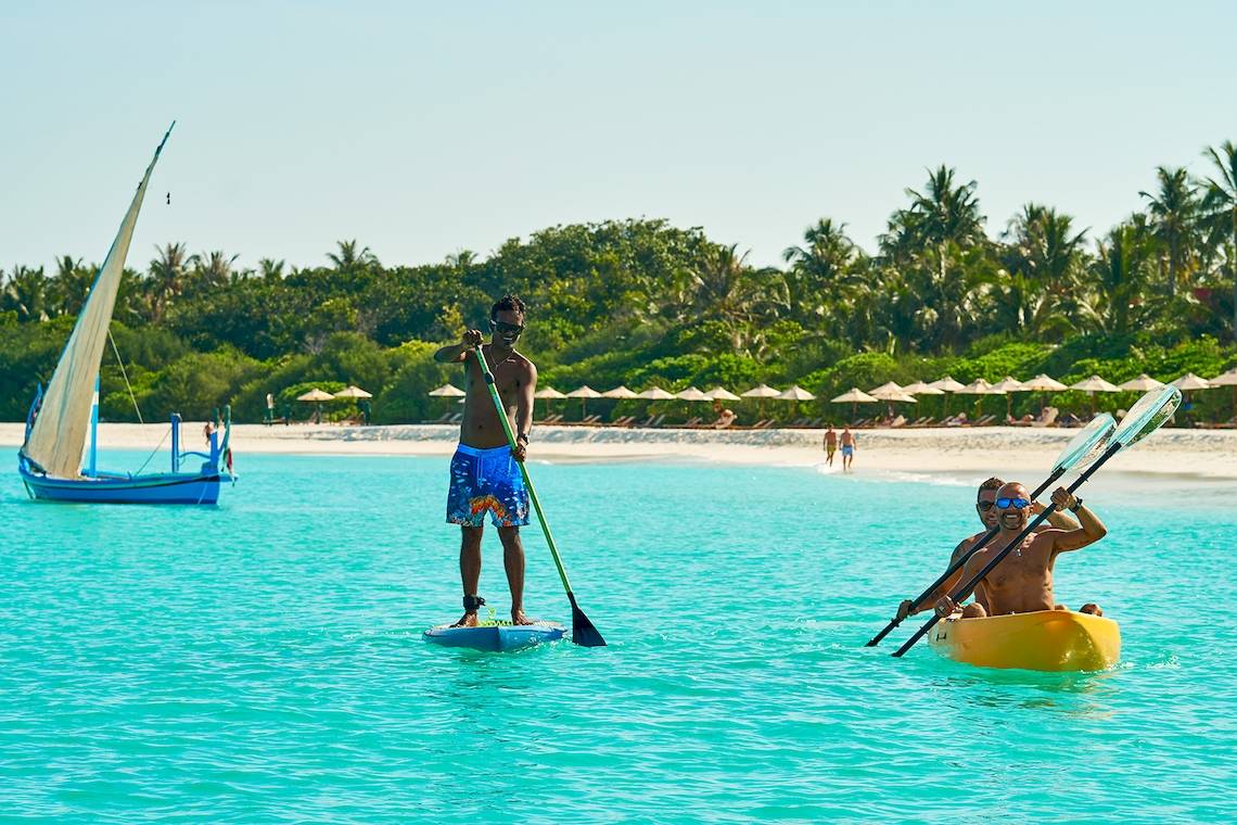 Zwei Männer paddeln auf dem Barefoot Eco Hotel, einer Segelboot ist im Hintergrund