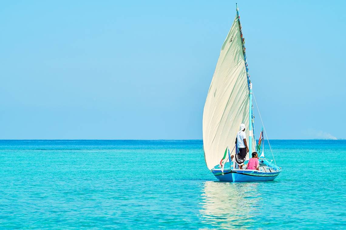 Ein Segelboot im Meer mit zwei Passagieren, einer steht und einer sitzt