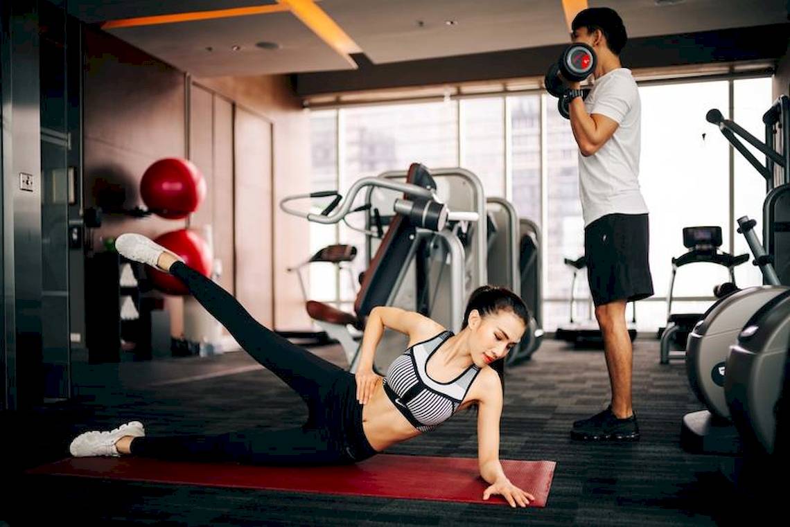 Frau mit Fitnesstrainer im Fitnessstudio, die Frau macht Liegestütze