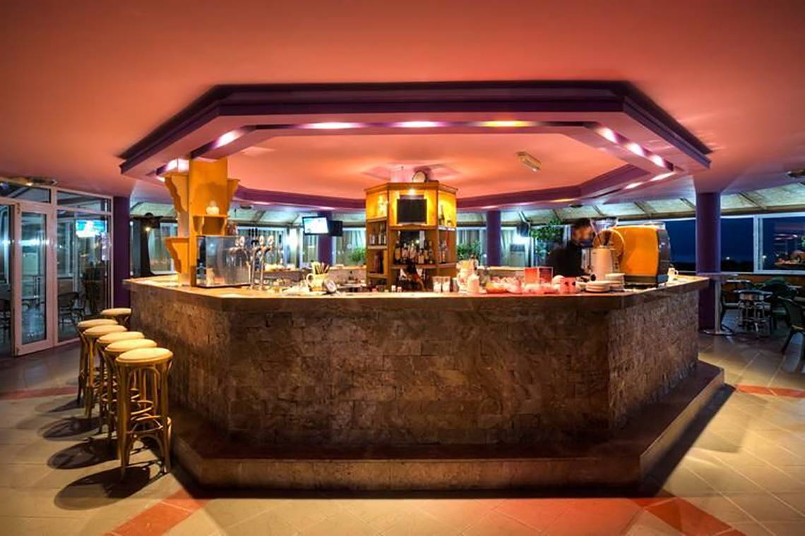Barbereich im Corali Hotel mit Steinwand und goldfarbenen Stühlen.