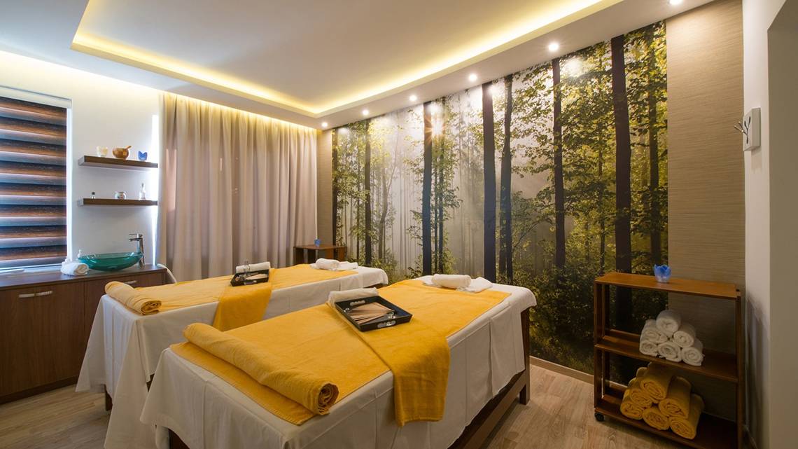 Spa-Behandlungsraum im Iberostar Creta Panorama & Mare Hotel mit zwei Massagetischen und einem großen Wandbild von Bäumen.