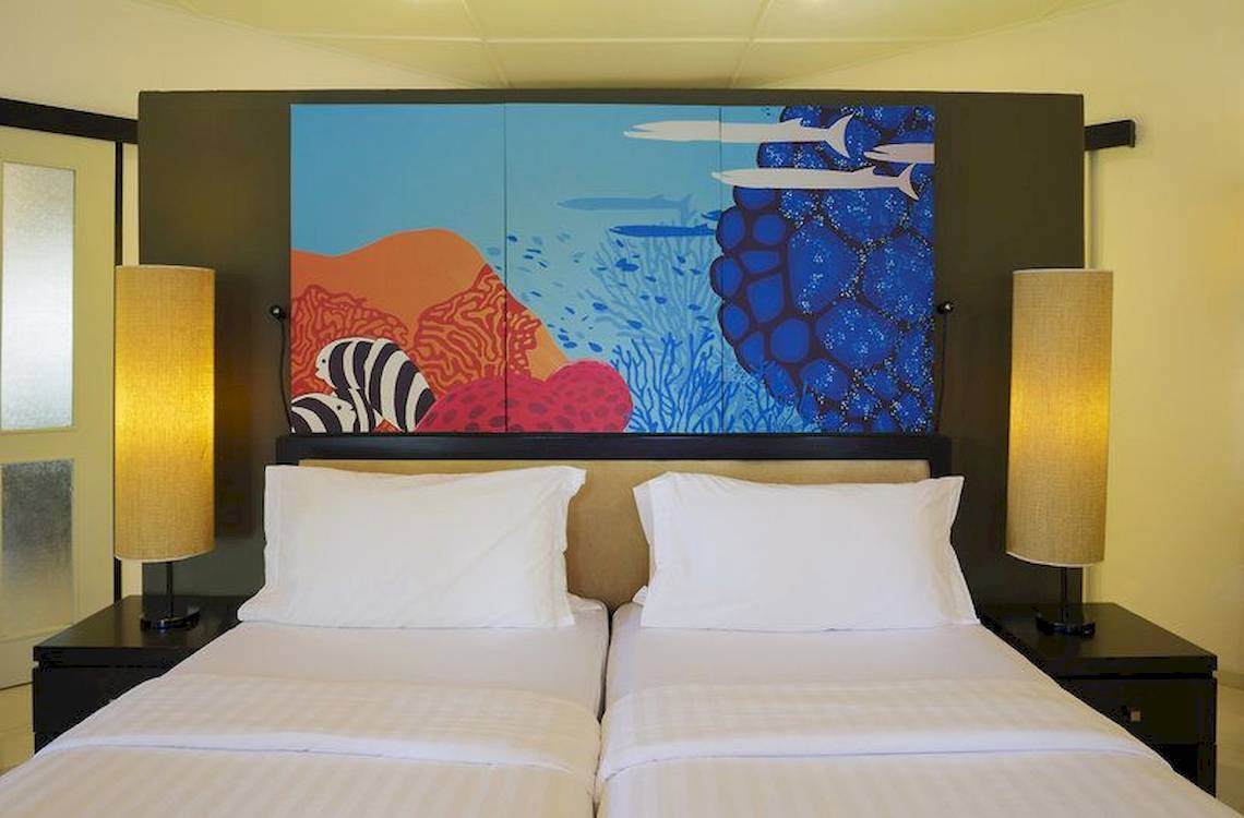 Doppelbett-Zimmer im Angsana Velavaru mit farbenfrohem Wandbild und zwei Nachttischen mit Lampen.