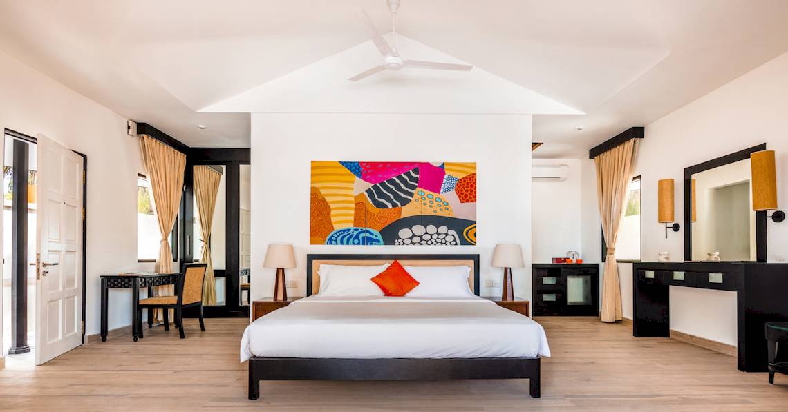 Schlafzimmer im Angsana Velavaru Hotel mit einem großen Bett, buntem Wandbild und weißen Wänden.