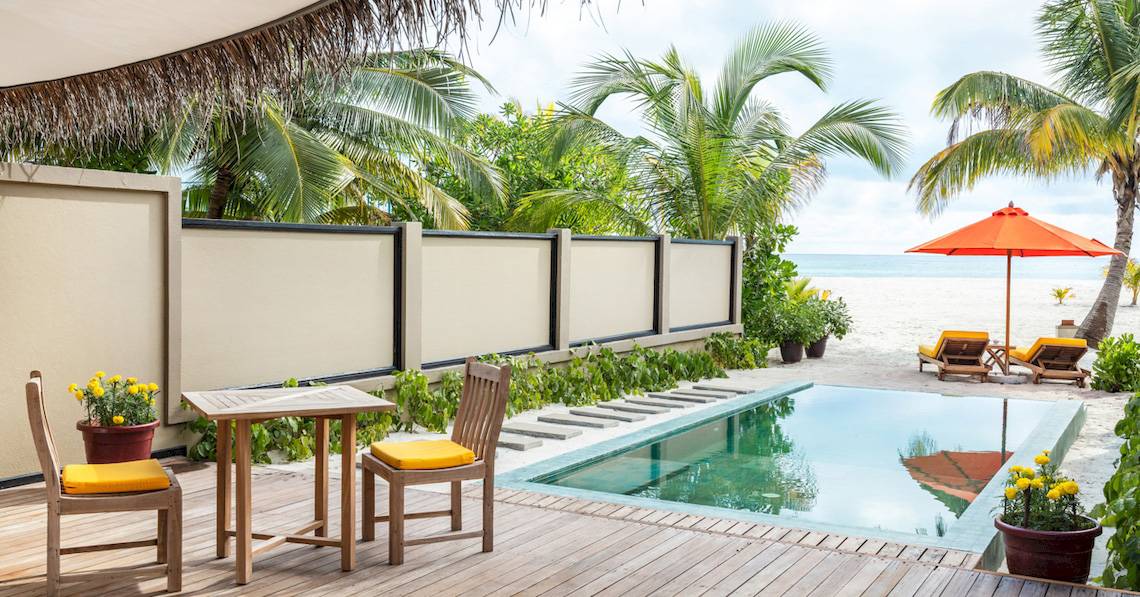 Außenbereich des Angsana Velavaru Hotels mit Pool, Tisch, Stühlen und Sonnenschirm am Strand