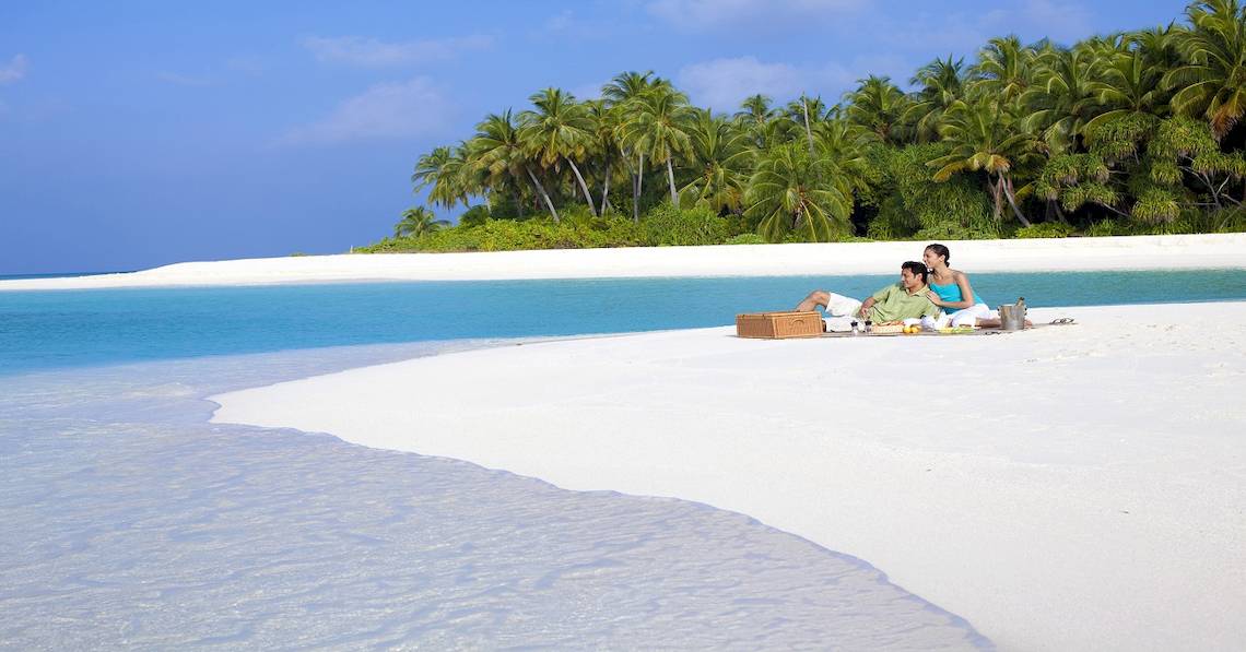 Paar sitzt auf weißem Sandstrand und genießt ein Picknick im Freien.