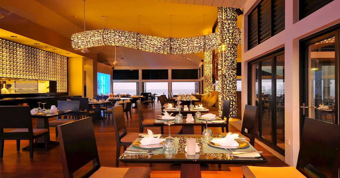 Innenansicht des Restaurants im Angsana Velavaru Hotel mit dekorativ beleuchteten Strukturen und offenen Türen zum Meer.
