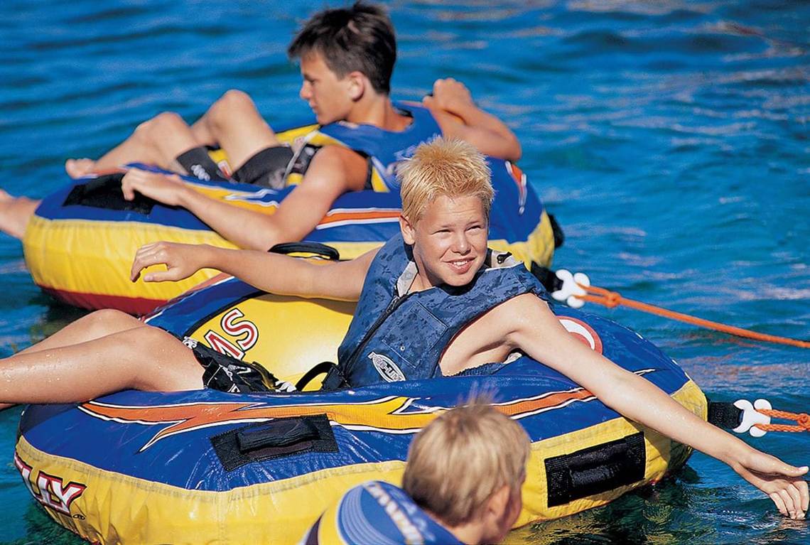 Drei Kinder schwimmen auf aufblasbaren Reifen im Wasser.