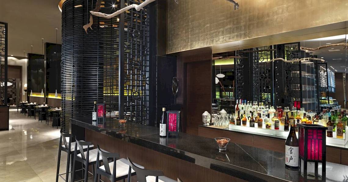 Innenansicht der Bar im Paradisus Playa del Carmen Hotel mit Tresen, Stühlen und vielen Getränkeflaschen.