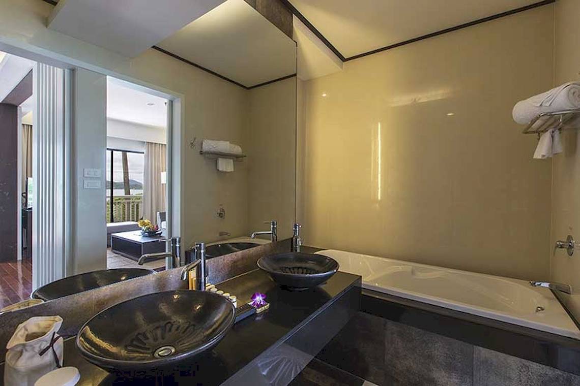 Badezimmer im Cape Panwa Hotel mit Badewanne, Spiegel und Waschbecken.
