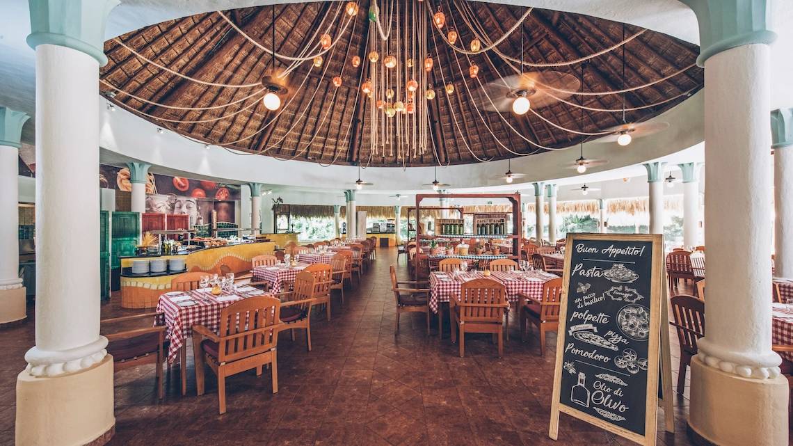 Innenansicht des Restaurants im Iberostar Paraiso del Mar Hotel mit vielen Tischen und Stühlen, einer Tafel und einer Kuppeldecke.