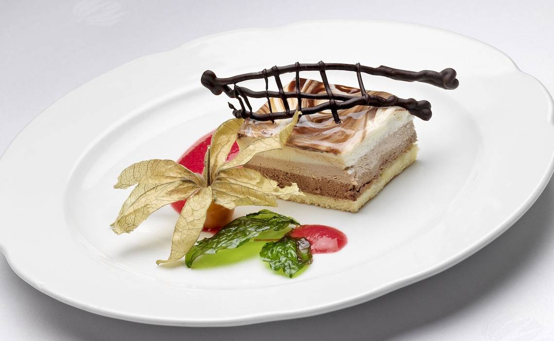 Dessert auf einem weißen Teller mit Schokoladen- und Fruchtdekoration.