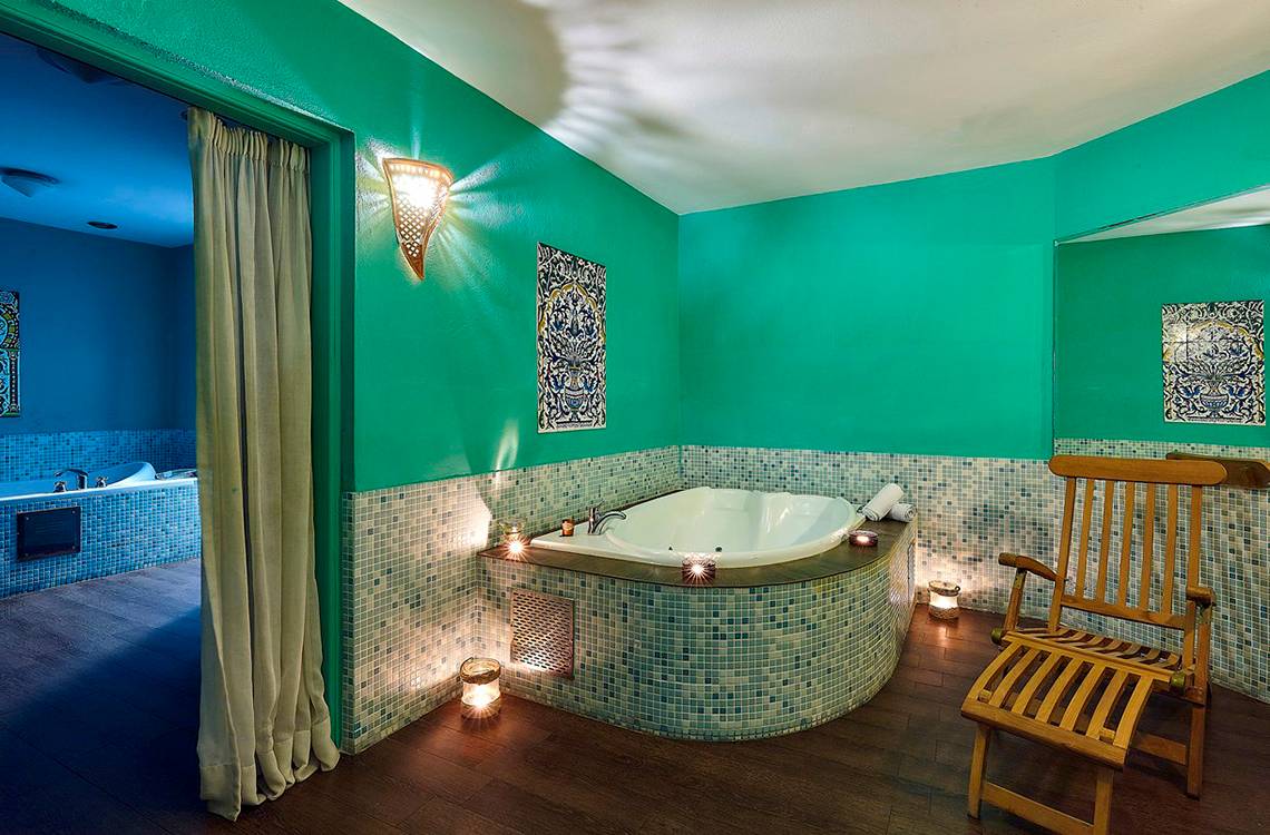 Badezimmer im Alexander Beach Hotel mit Badewanne, Holzstuhl und grünen Wänden.