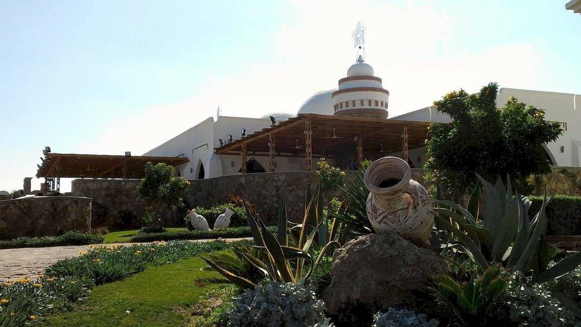 Außenansicht des Gorgonia Beach Resorts mit weißem Gebäude, Kuppel und Gartenanlage.