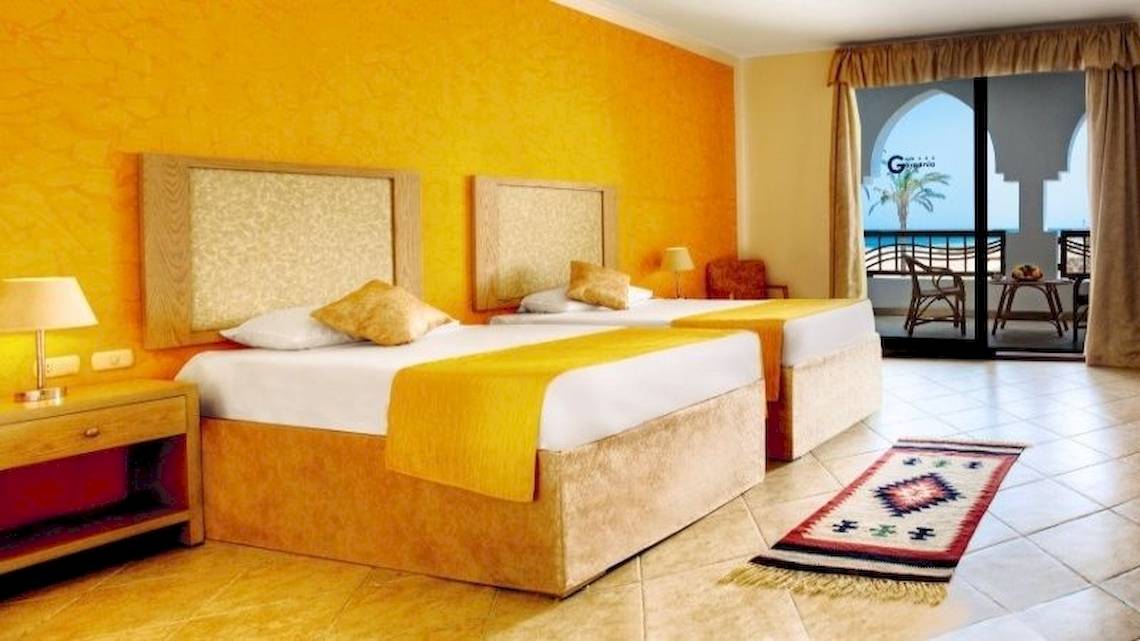 Zwei Betten in einem Hotelzimmer mit gelben Wänden, einem Balkon und Meerblick.