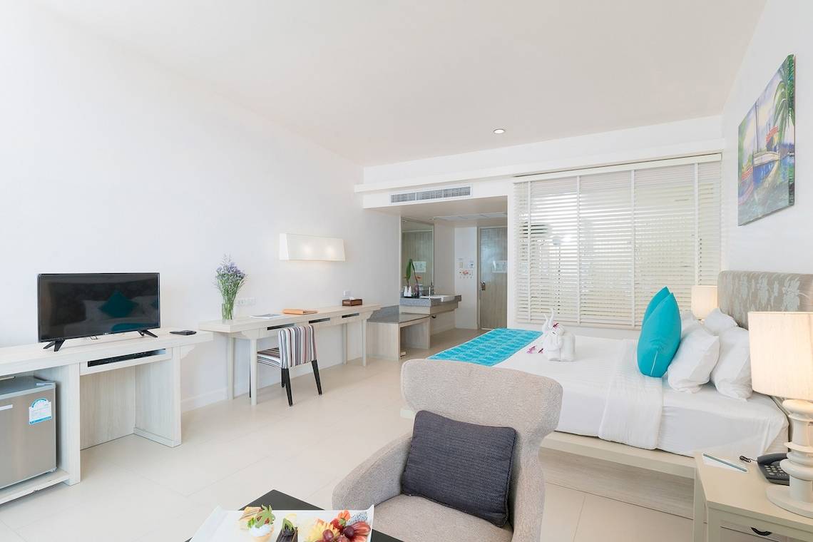 Das moderne Hotelzimmer im Briza Beach Resort mit Fernseher, Schreibtisch, Sessel, Bett und Obstplatte.