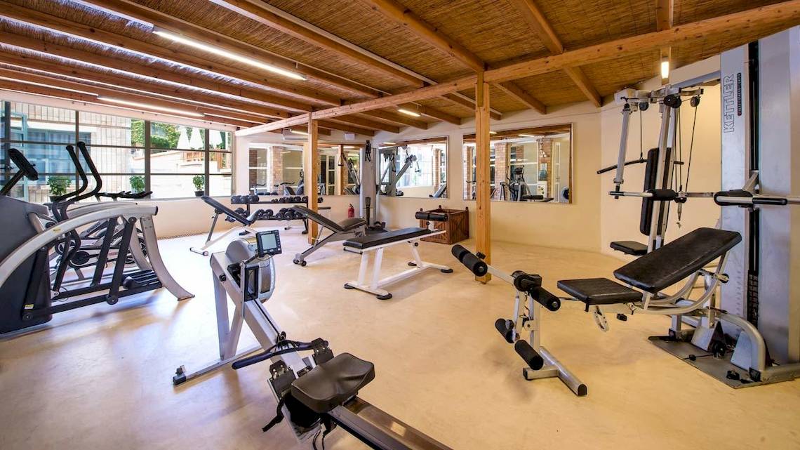 Fitnessraum im Bella Beach Hotel mit verschiedenen Trainingsgeräten und Holzbalkendecke.
