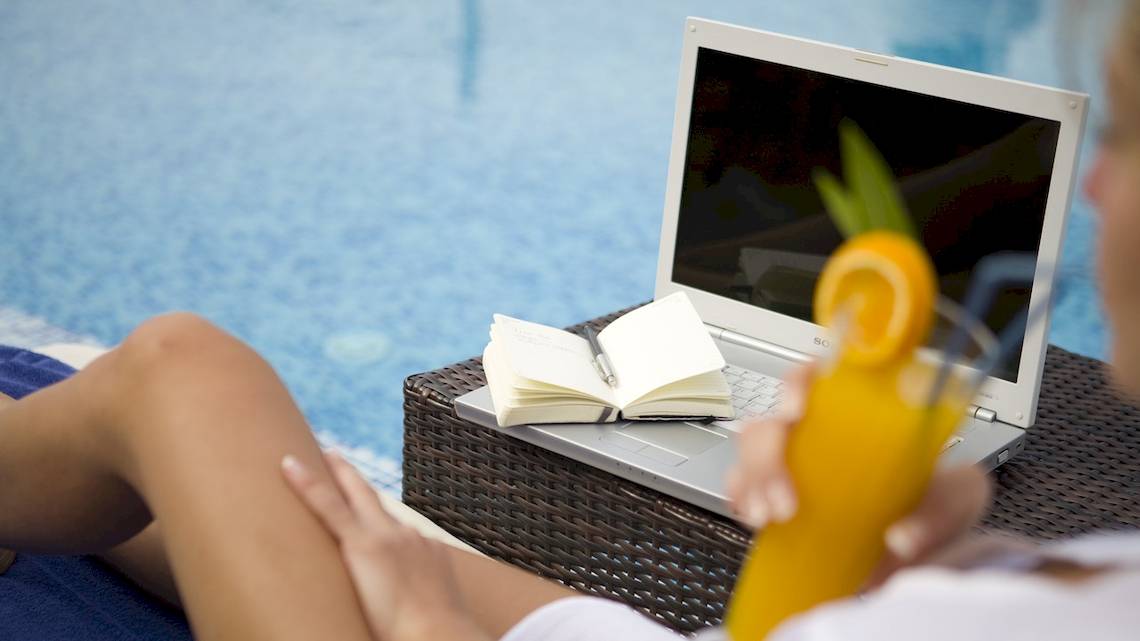 Frau am Pool mit Laptop und Buch