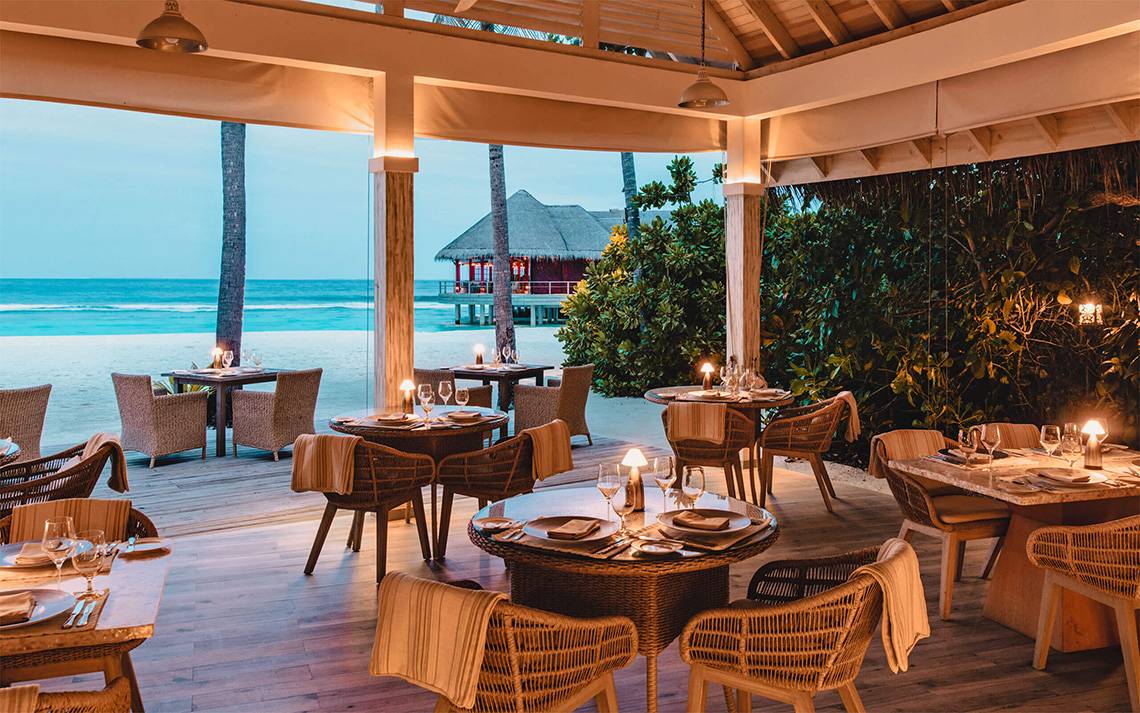 Außenbereich des Finolhu Baa Atoll Maldives Hotels mit Tischen und Stühlen am Meer.
