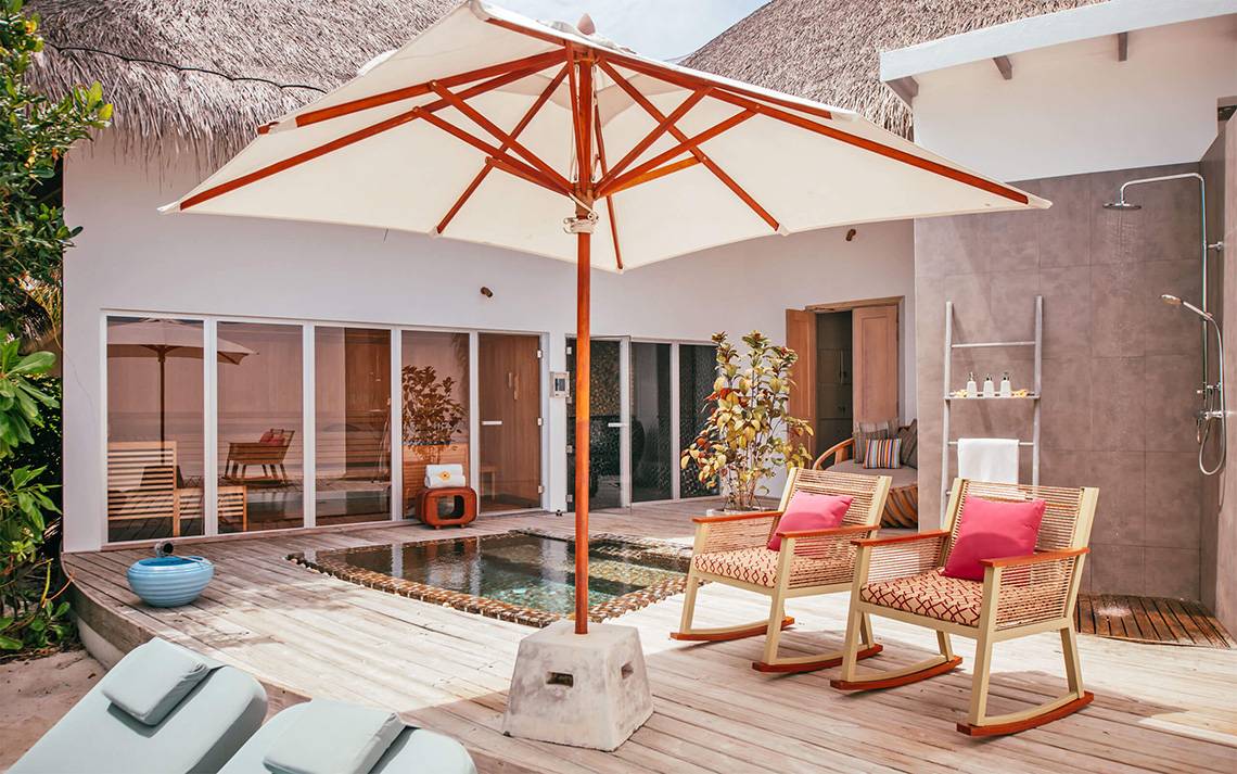 Außenbereich des Finolhu Baa Atoll Maldives Hotels mit Terrasse, weißem Sonnenschirm und zwei Sesseln.