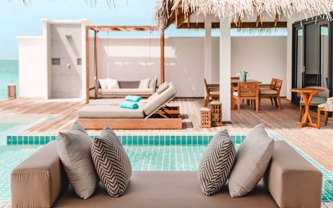 Loungebereich am Pool mit Sonnenliegen, Tisch und überdachter Veranda im Finolhu Baa Atoll Maldives Hotel.